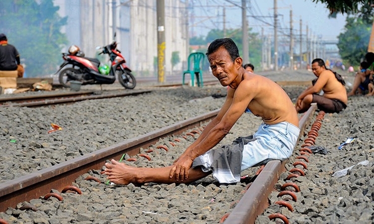 Người Indonesia ngồi trên đường ray tàu hỏa tắm nắng ở Bekasi, Tây Java, hôm 4/4. Ảnh: AFP.