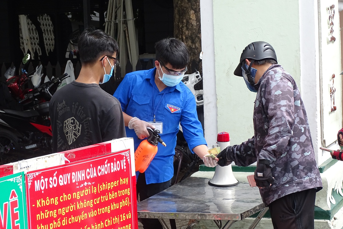 Tình nguyện viên phun khử khuẩn hàng hóa, tiền thừa từ nhân viên giao hàng. Ảnh: Hà An.